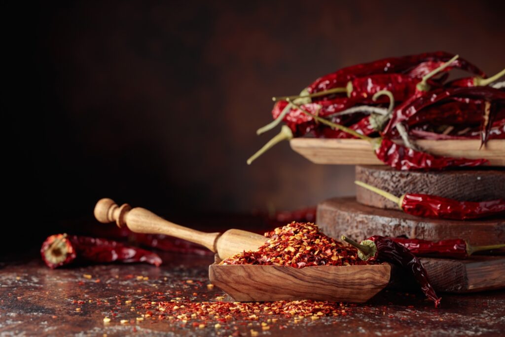 Chilli flakes and dried chili peppers on a brown table. Image Via Shutterstock